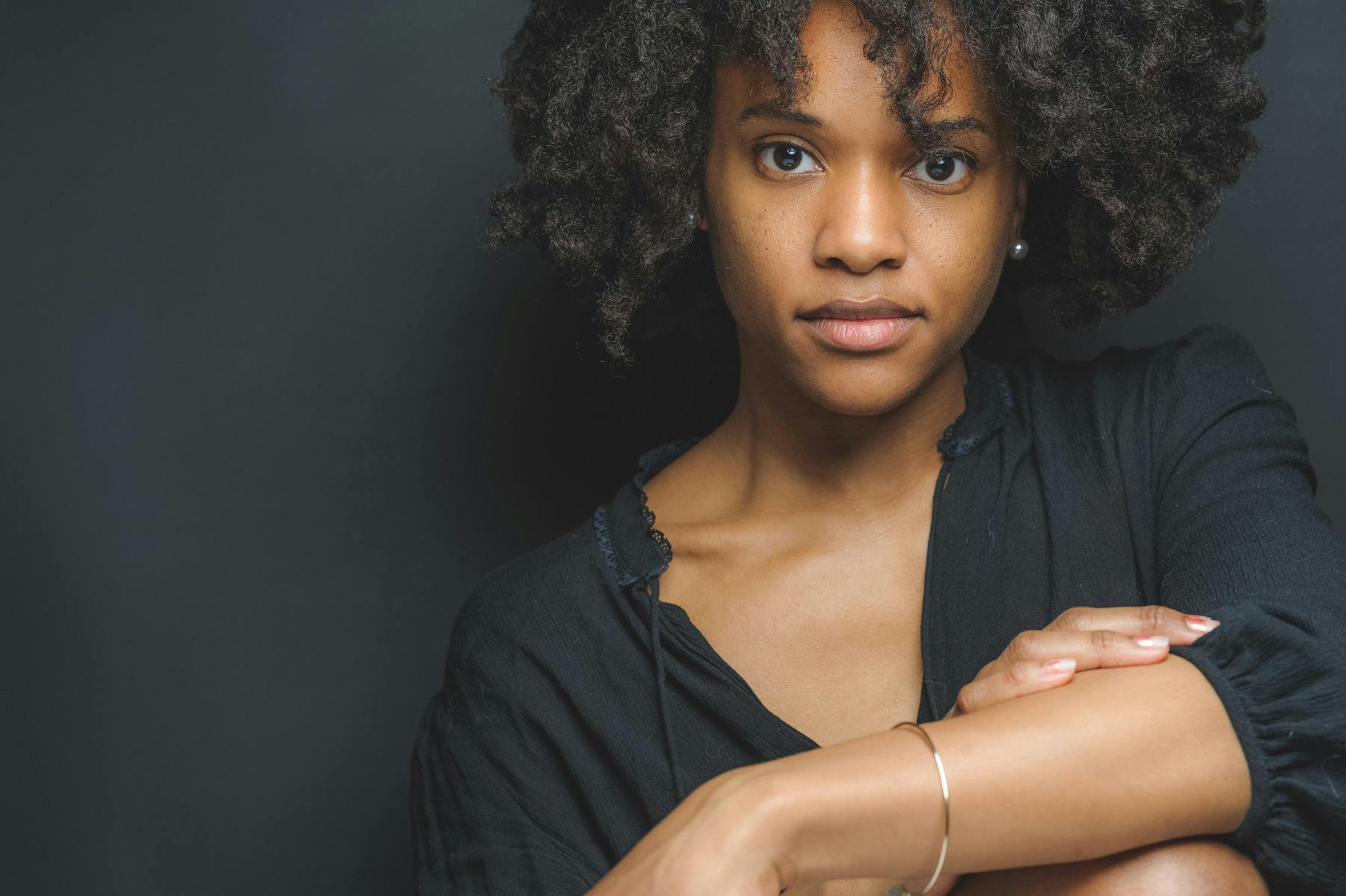 portrait of photographer and dancer Michelle Reid sitting in front of a black background wearing a black top with a gold bracelet on her wrist.