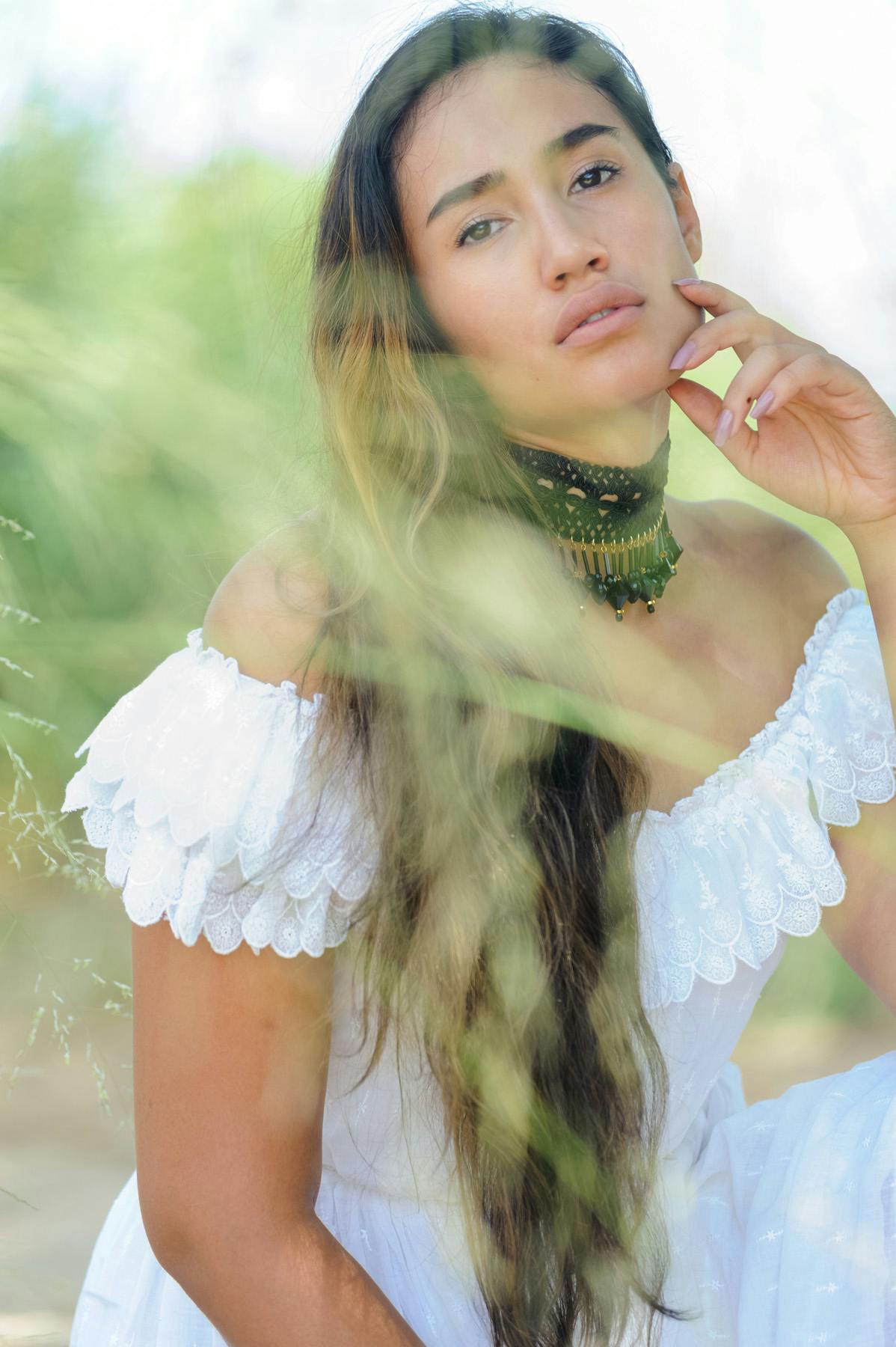 portrait of Shari, a woman wearing a white dress with long brown hair with tall green grass blurred in front of her