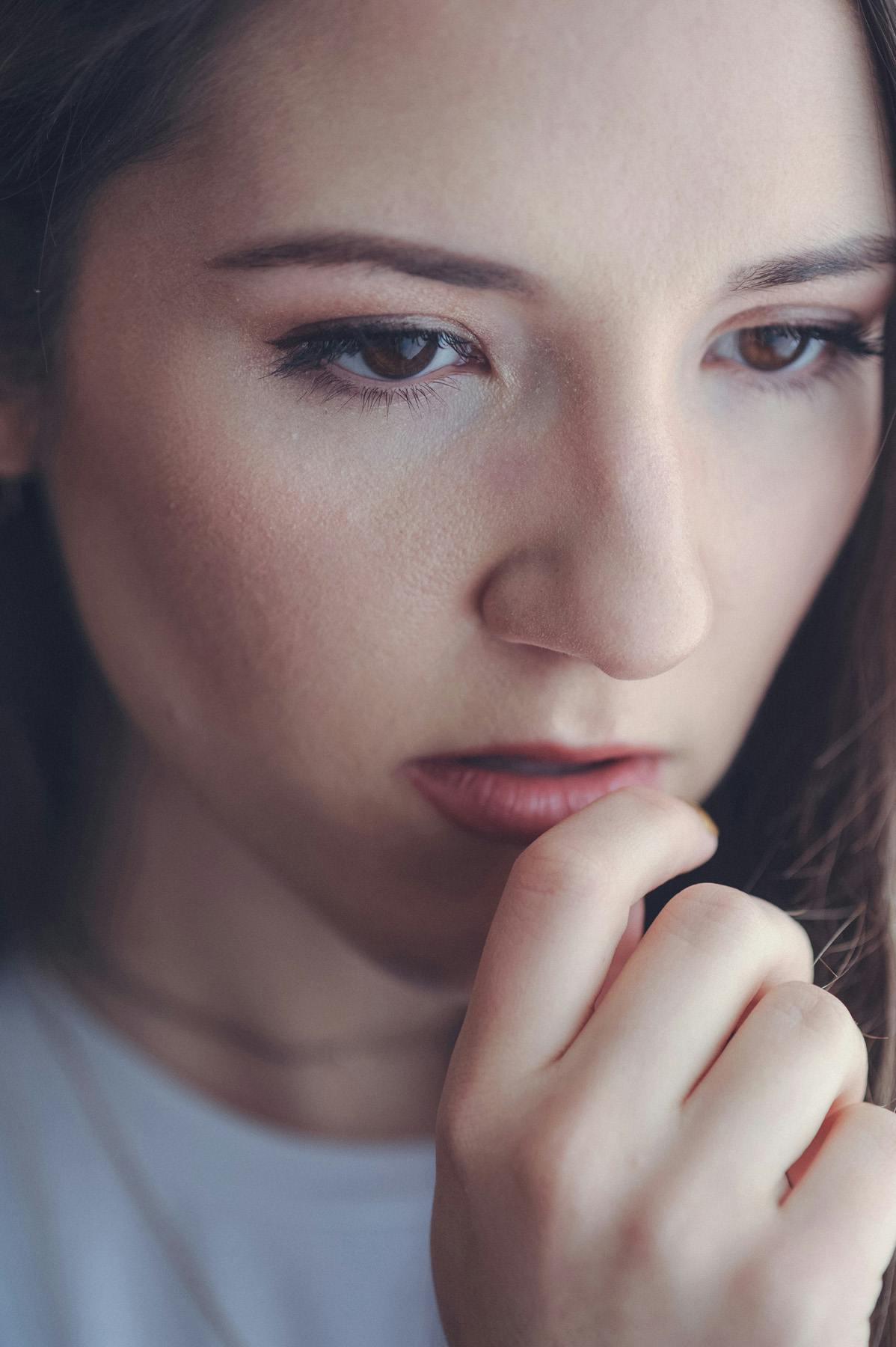 a closeup portrait of Ania with her hand to her face looking down pensively. 