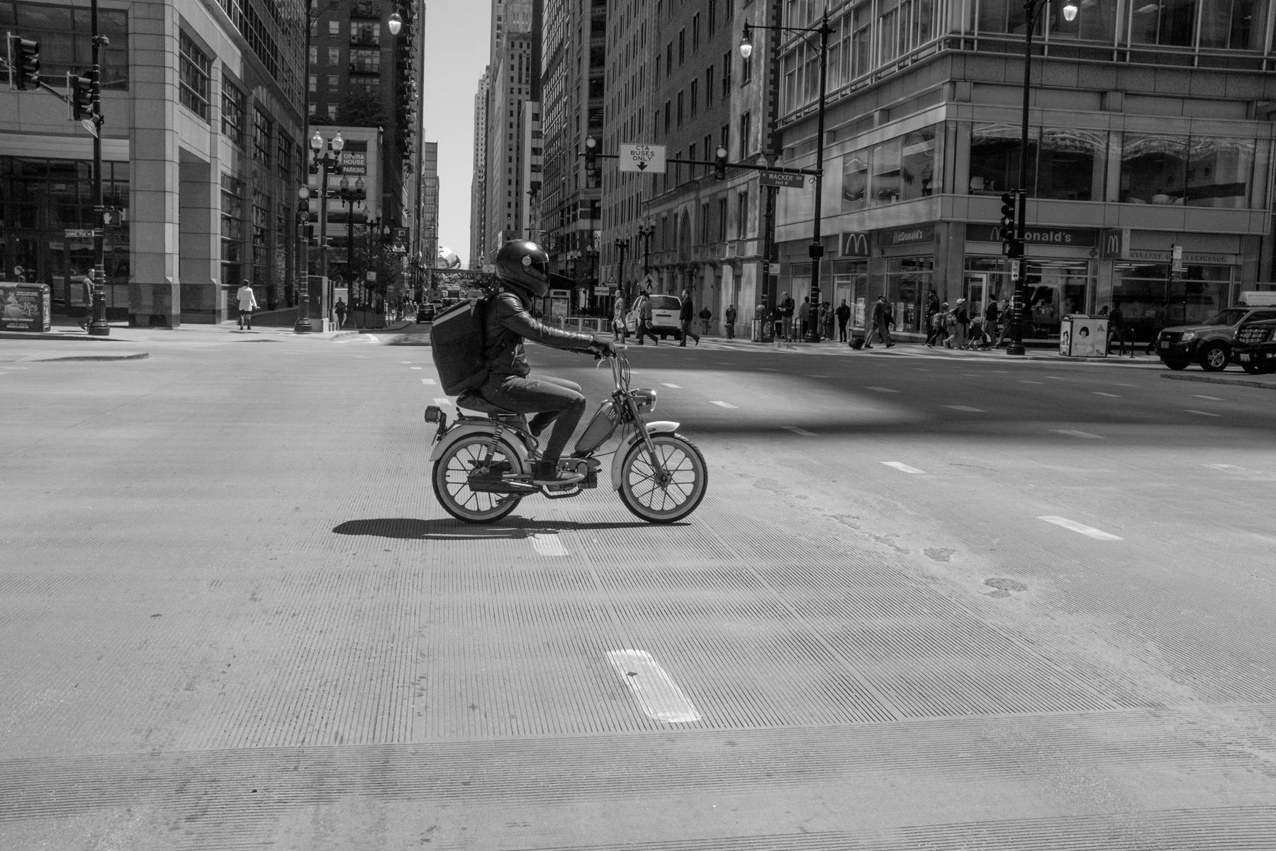 a motorcycle helmet wearing commuter riding a moped in downtown chicago.