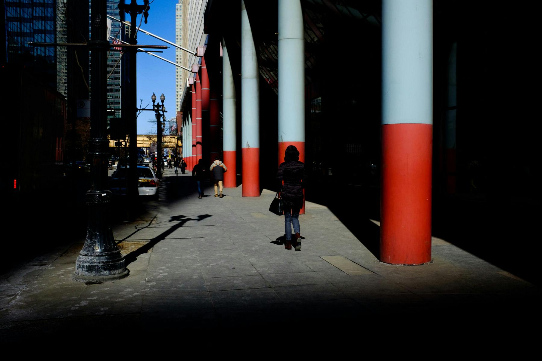 woman standing near the blue and red pillars of the Thompson Center surrounded by deep shadows.