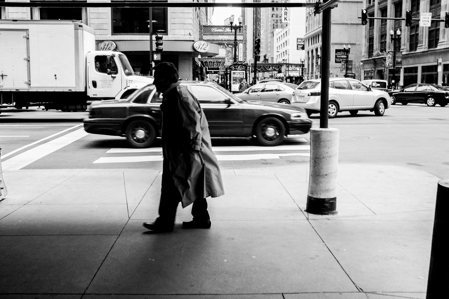 a black and white shot of an older gentleman in deep shadow walking in downtown Chicago with a slight slouch.