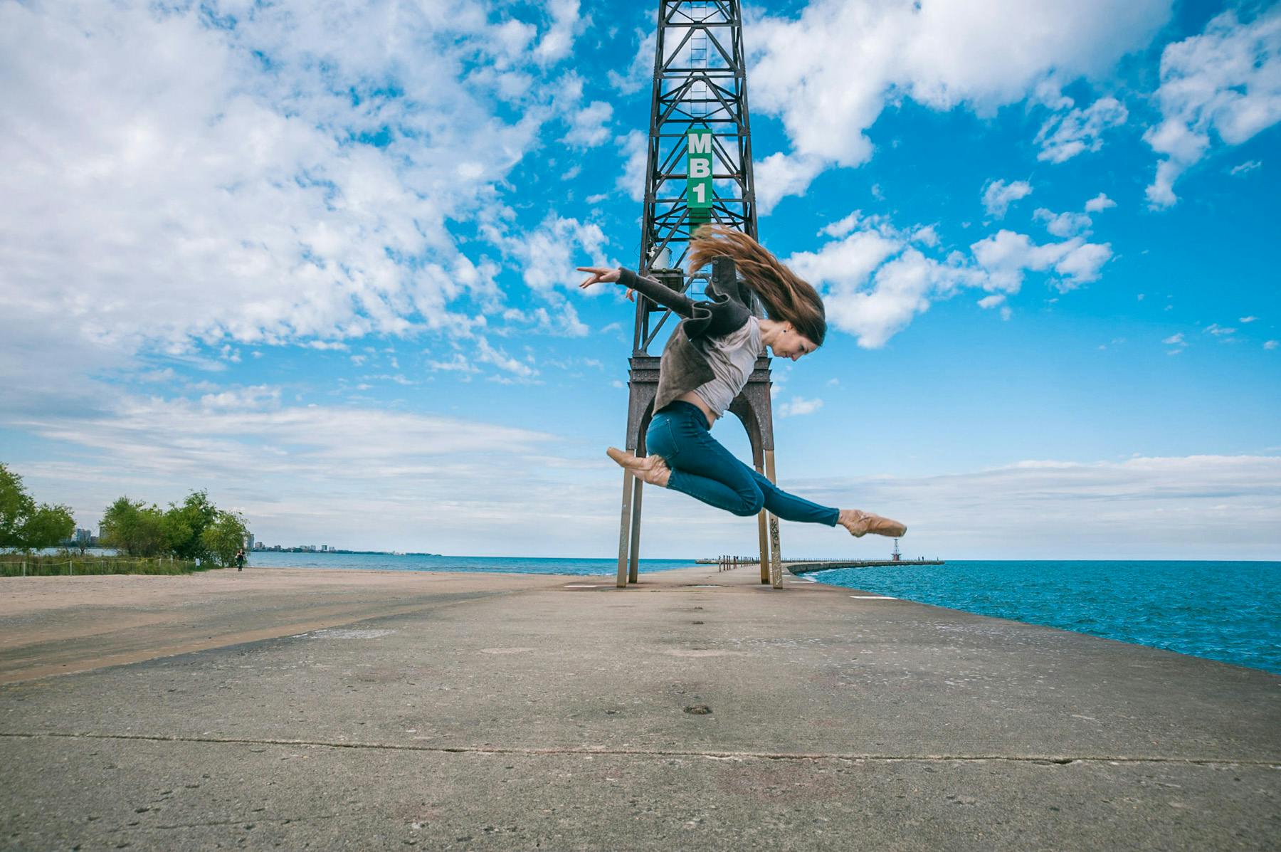 photo of dancer Elizabeth Cohen in mid air on a dock in Chicago with a beautifully blue cloudy sky and a tower in the background